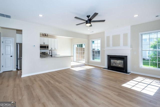 2915 Commonwealth Cir, Alpharetta, GA 30004 - unfurnished living room with light wood finished floors, a ceiling fan, a glass covered fireplace, baseboards, and recessed lighting