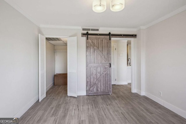 2285 Peachtree Rd NE, Atlanta, GA 30309 - unfurnished bedroom with crown molding, wood finished floors, a barn door, baseboards, and a walk in closet
