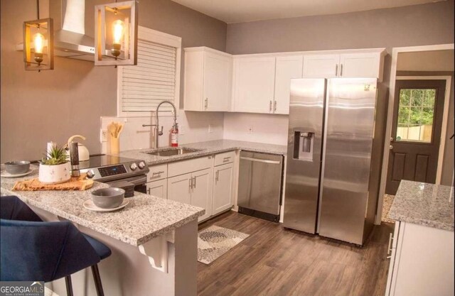 836 Wood St NW, Atlanta, GA 30318 - kitchen featuring appliances with stainless steel finishes, wall chimney exhaust hood, white cabinets, dark wood-style flooring, and a peninsula
