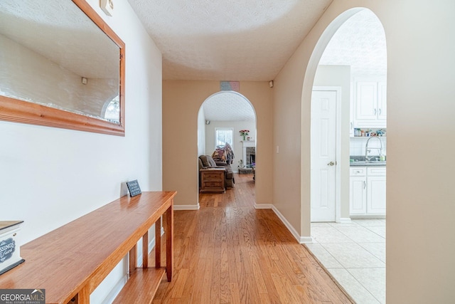 704 Stonecrest Ln, Loganville, GA 30052 - hallway with arched walkways, light wood-type flooring, a textured ceiling, a sink, and baseboards