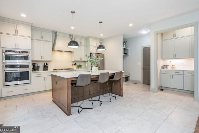 1013 Liberty Springs Dr, Woodstock, GA 30188 - kitchen featuring stainless steel appliances, light countertops, a kitchen breakfast bar, premium range hood, and a kitchen island with sink