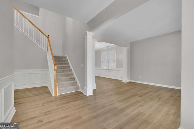 955 Mill Creek Ave, Canton, GA 30115 - unfurnished living room featuring stairway, ornate columns, light wood-style floors, a decorative wall, and a wainscoted wall
