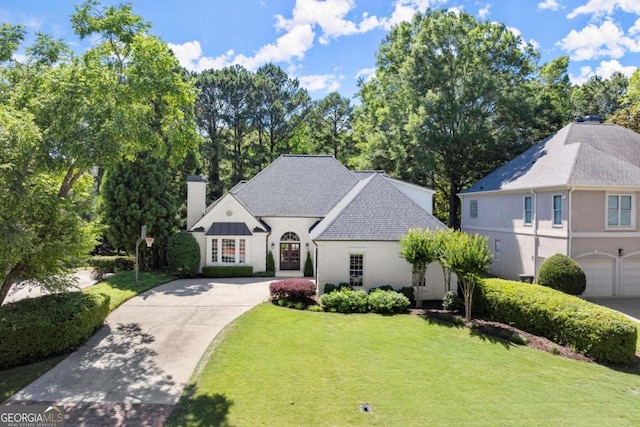5120 Falcon Chase Ln, Atlanta, GA 30342 - french country home featuring a chimney, driveway, a front lawn, stucco siding, and a shingled roof