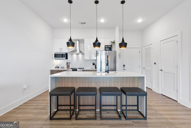 112 Rogers St NE Unit 410, Atlanta, GA 30317 - kitchen with wall chimney exhaust hood, stainless steel appliances, white cabinetry, a kitchen bar, and a kitchen island with sink
