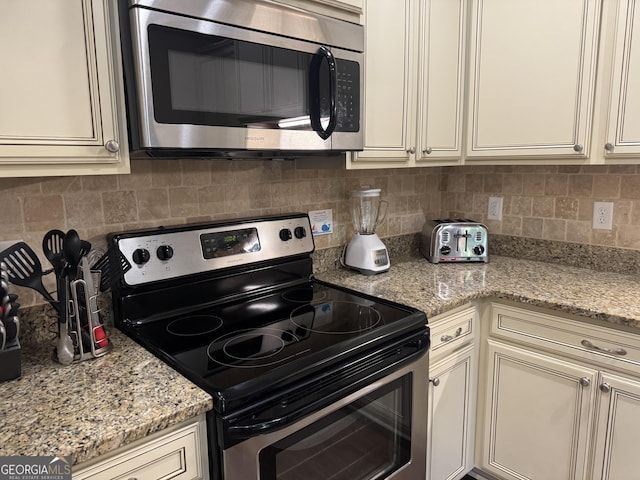 306 Reserve Ln, Saint Simons, GA 31522 - kitchen featuring stainless steel appliances, backsplash, cream cabinets, and light stone countertops