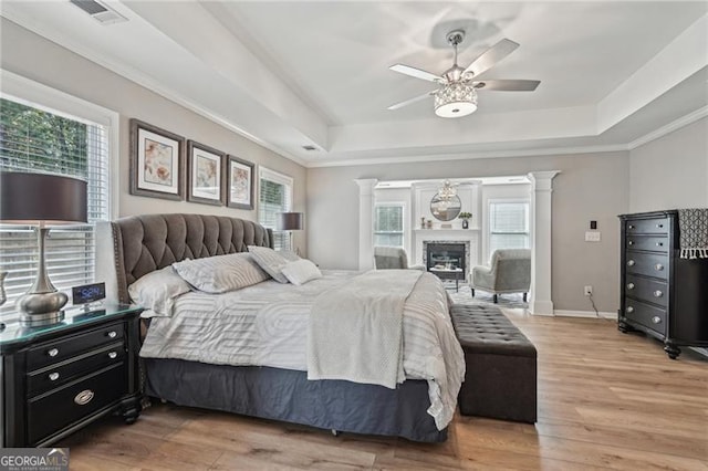 1017 Preserve Park Dr, Loganville, GA 30052 - bedroom featuring a raised ceiling, decorative columns, light wood-style flooring, crown molding, and a glass covered fireplace