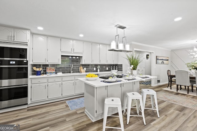 1143 Mcgarity Rd, Mcdonough, GA 30252 - kitchen featuring appliances with stainless steel finishes, light countertops, a kitchen bar, ornamental molding, and light wood finished floors
