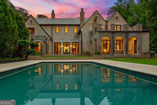 4560 Harris Trl, Atlanta, GA 30327 - back of property at dusk with a balcony, french doors, stone siding, an outdoor pool, and a chimney