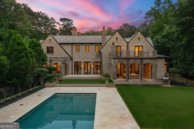 4560 Harris Trl, Atlanta, GA 30327 - back of property at dusk featuring a balcony, stone siding, a chimney, and a patio