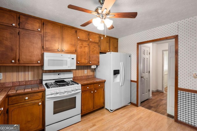 2617 Laurel Woods Ln SE, Conyers, GA 30094 - kitchen with white appliances, wallpapered walls, tile countertops, brown cabinetry, and ceiling fan