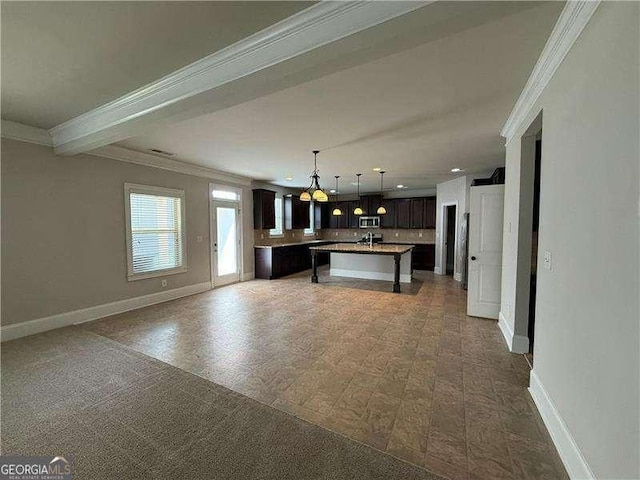 3488 Woodshade Dr, Loganville, GA 30052 - kitchen featuring ornamental molding, a kitchen island with sink, baseboards, open floor plan, and dark brown cabinets
