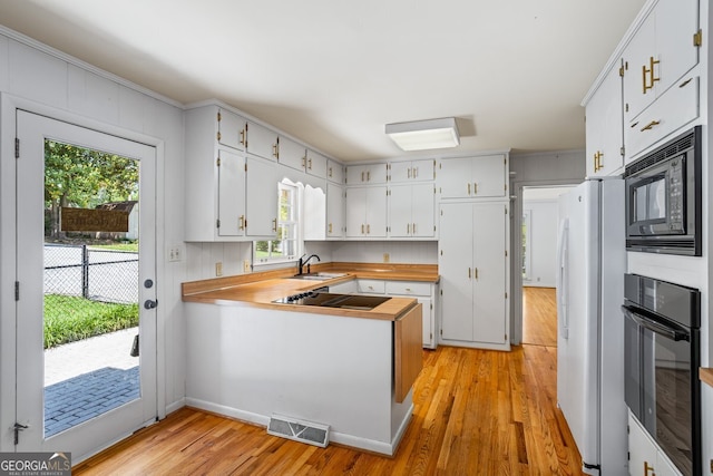7121 Forest Dr SE, Covington, GA 30014 - kitchen with black appliances, light wood-style flooring, a peninsula, white cabinetry, and butcher block countertops