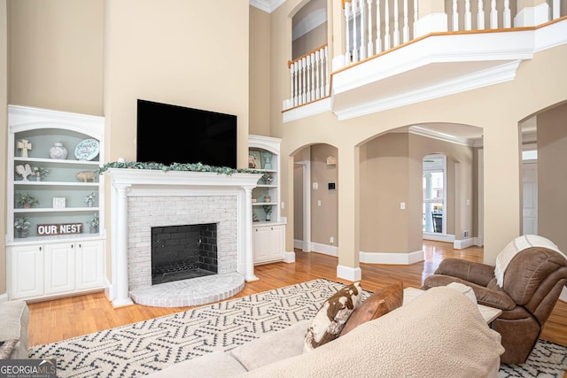 395 Grove Ridge Dr, Loganville, GA 30052 - living room featuring a towering ceiling, arched walkways, light wood-type flooring, built in features, and a brick fireplace