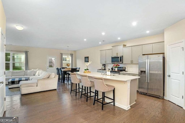 105 Paulowina Cir, Mcdonough, GA 30253 - kitchen with stainless steel appliances, a breakfast bar area, a center island with sink, light countertops, and dark wood-style flooring