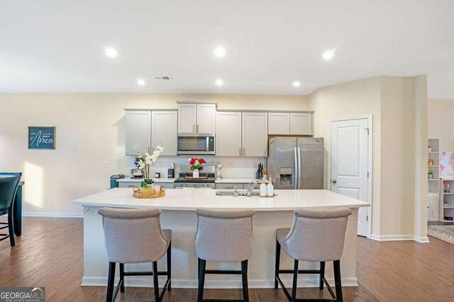 105 Paulowina Cir, Mcdonough, GA 30253 - kitchen featuring appliances with stainless steel finishes, a kitchen island with sink, a breakfast bar area, a sink, and tasteful backsplash