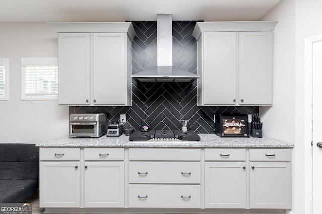 646 Mccarley Downs Dr, Bonaire, GA 31005 - kitchen featuring wall chimney range hood, tasteful backsplash, stainless steel gas cooktop, white cabinets, and light stone countertops