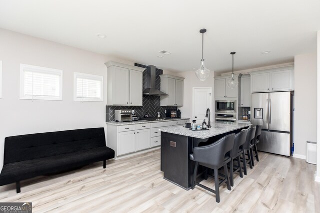 646 Mccarley Downs Dr, Bonaire, GA 31005 - kitchen with appliances with stainless steel finishes, wall chimney range hood, decorative backsplash, a breakfast bar area, and light wood-type flooring