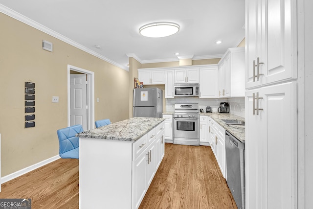 827 Fraser St SE, Atlanta, GA 30315 - kitchen featuring stainless steel appliances, light wood-style flooring, ornamental molding, white cabinets, and a center island