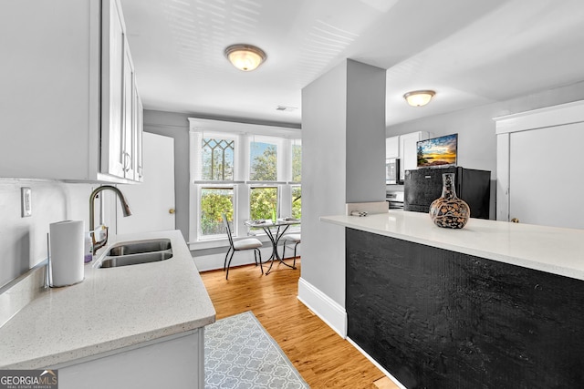 1021 Oak St SW, Atlanta, GA 30310 - kitchen with a sink, white cabinetry, light wood-type flooring, stainless steel microwave, and baseboards