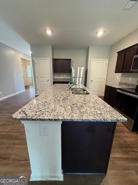 170 Forray Dr, Covington, GA 30016 - kitchen featuring appliances with stainless steel finishes, a sink, light stone countertops, a center island with sink, and dark brown cabinetry