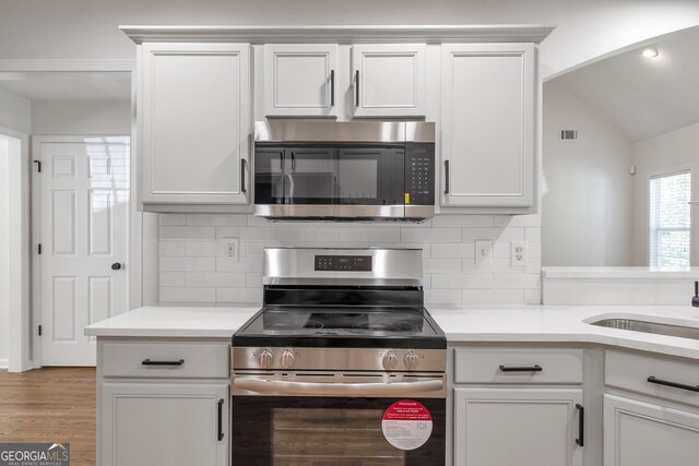 5523 River Valley Way, Flowery Branch, GA 30542 - kitchen featuring appliances with stainless steel finishes, backsplash, light countertops, light wood finished floors, and vaulted ceiling