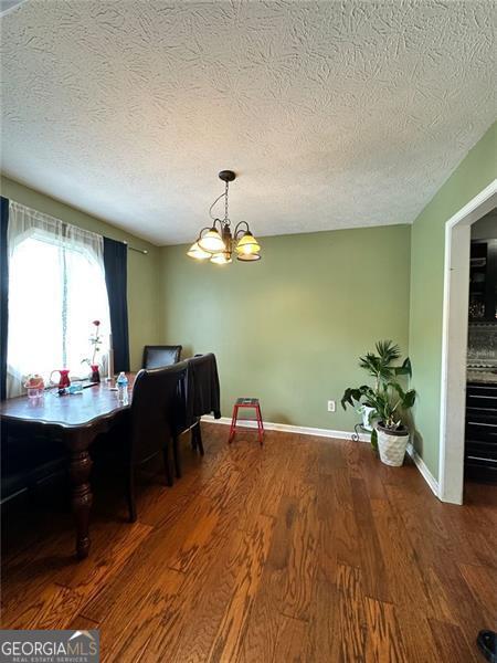 2816 Quinbery Dr, Snellville, GA 30039 - dining area featuring wood finished floors, a chandelier, a textured ceiling, and baseboards