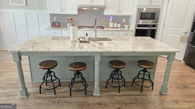 2321 Margaux Ct, Monroe, GA 30656 - kitchen featuring stainless steel appliances, under cabinet range hood, white cabinets, a breakfast bar, and a wainscoted wall