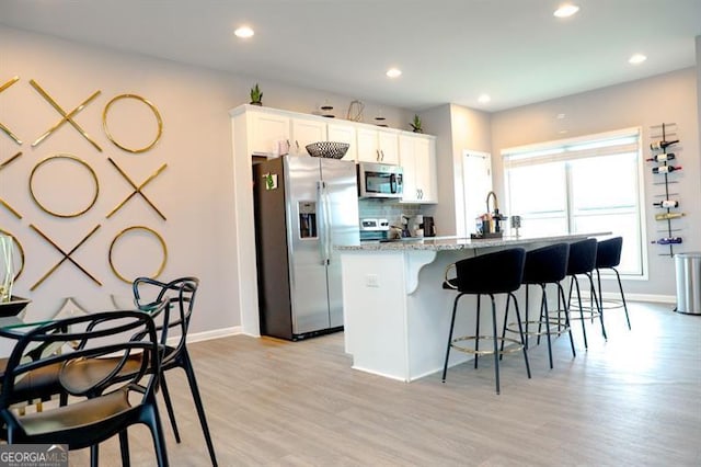 3615 Hawthorne Ter, Atlanta, GA 30337 - kitchen featuring stainless steel appliances, light wood-style floors, a breakfast bar area, a kitchen island with sink, and light stone countertops