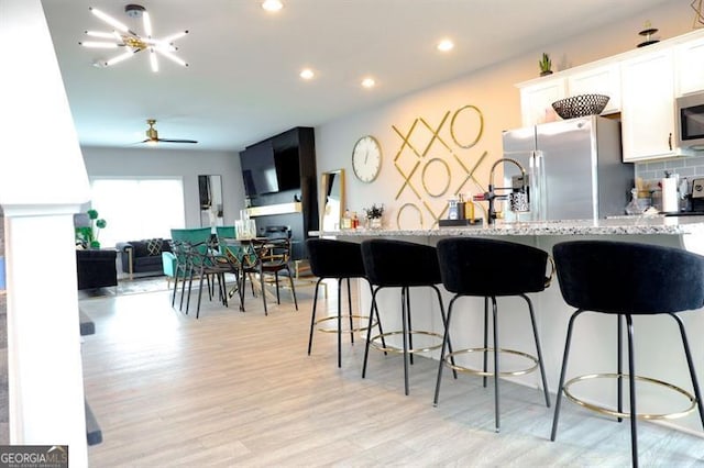 3615 Hawthorne Ter, Atlanta, GA 30337 - kitchen featuring appliances with stainless steel finishes, white cabinetry, light stone countertops, a kitchen bar, and light wood-style flooring
