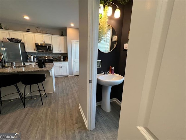 3615 Hawthorne Ter, Atlanta, GA 30337 - kitchen with appliances with stainless steel finishes, wood finished floors, white cabinetry, backsplash, and a kitchen bar