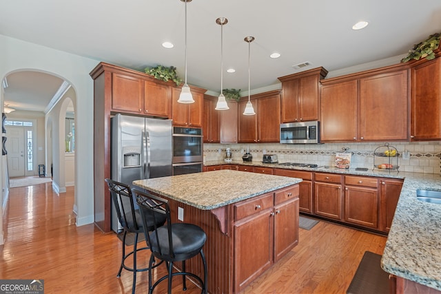 3476 Bridge Walk Dr, Lawrenceville, GA 30044 - kitchen with stainless steel appliances, arched walkways, a kitchen island, decorative backsplash, and light stone countertops