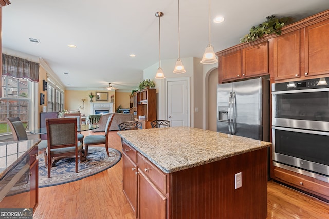 3476 Bridge Walk Dr, Lawrenceville, GA 30044 - kitchen with stainless steel appliances, light wood-type flooring, a kitchen island, a fireplace, and decorative light fixtures