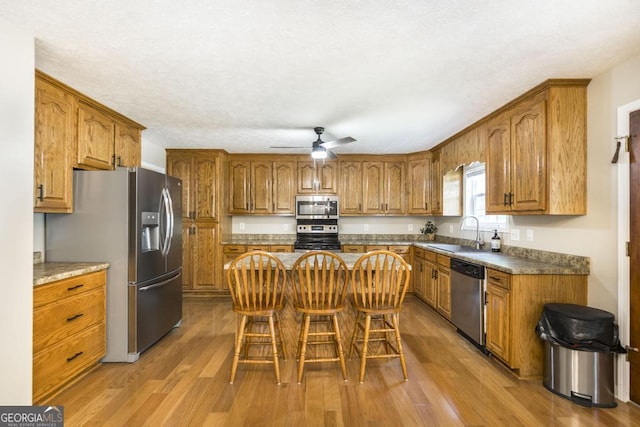 4407 Jones Rd, Macon, GA 31216 - kitchen with stainless steel appliances, a sink, brown cabinets, light wood-style floors, and a textured ceiling