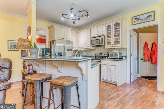 211 Westwood Dr, Calhoun, GA 30701 - kitchen featuring appliances with stainless steel finishes, a kitchen breakfast bar, dark countertops, light wood-style floors, and glass insert cabinets