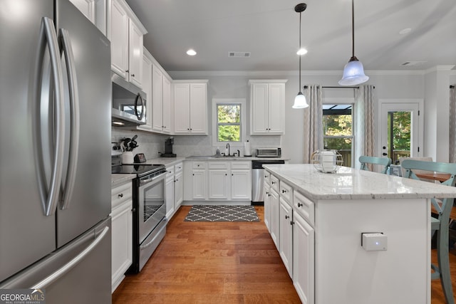 1412 Short Ct, Mcdonough, GA 30252 - kitchen featuring appliances with stainless steel finishes, a kitchen breakfast bar, wood finished floors, ornamental molding, and a kitchen island