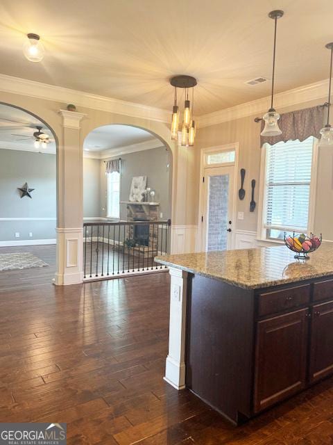 1869 Schofield Dr, Hampton, GA 30228 - kitchen featuring arched walkways, dark brown cabinetry, light stone countertops, a ceiling fan, and crown molding
