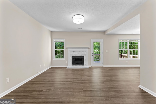 80 Corn Row Ct, Newnan, GA 30263 - unfurnished living room featuring plenty of natural light, a textured ceiling, a fireplace with raised hearth, and dark wood-type flooring