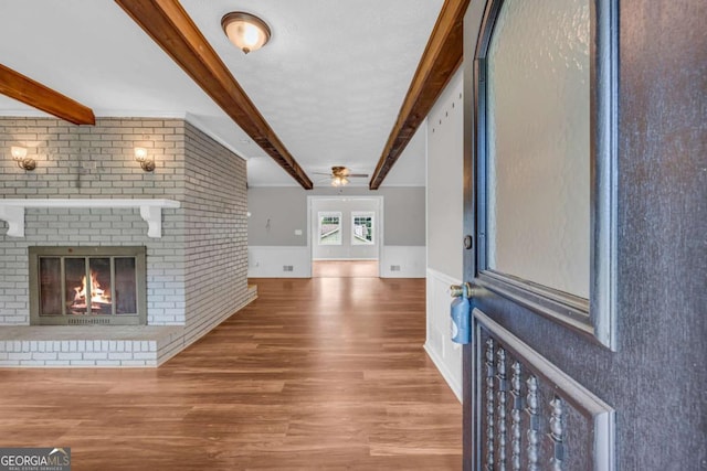 3642 S Bogan Rd, Buford, GA 30519 - unfurnished living room featuring beam ceiling, wood finished floors, ceiling fan, wainscoting, and a fireplace
