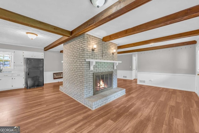 3642 S Bogan Rd, Buford, GA 30519 - unfurnished living room featuring beam ceiling, a fireplace, light wood-style flooring, and a wainscoted wall