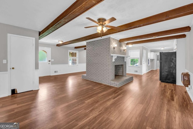 3642 S Bogan Rd, Buford, GA 30519 - unfurnished living room with a ceiling fan, beam ceiling, wood finished floors, a brick fireplace, and a wainscoted wall