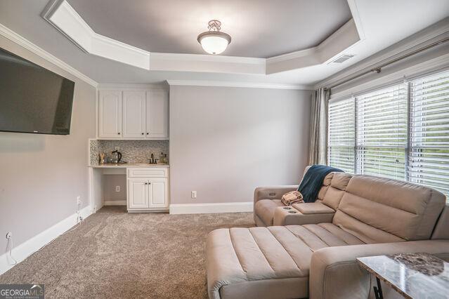 4818 Moon Hollow Ct, Buford, GA 30519 - living area with a raised ceiling, ornamental molding, light colored carpet, baseboards, and wet bar