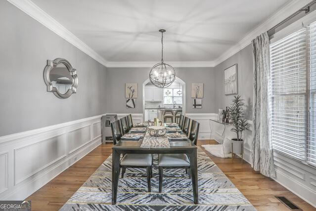 4818 Moon Hollow Ct, Buford, GA 30519 - dining area featuring a chandelier, wood finished floors, ornamental molding, a decorative wall, and a wainscoted wall