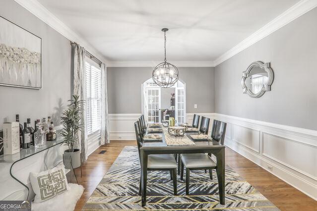 4818 Moon Hollow Ct, Buford, GA 30519 - dining area featuring a chandelier, crown molding, wood finished floors, a wainscoted wall, and a decorative wall