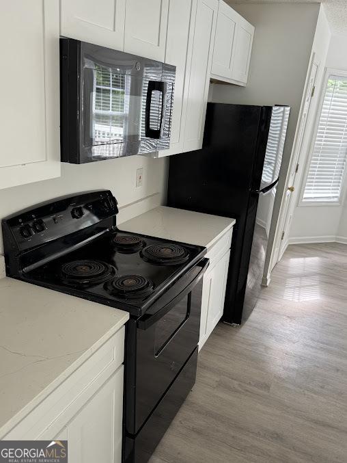 5709 Newnan Cir, Austell, GA 30106 - kitchen with black appliances, white cabinetry, light wood finished floors, and light stone counters