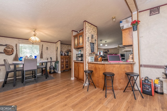 206 Briar Creek Way, Lizella, GA 31052 - kitchen featuring wood finished floors, brown cabinets, a textured ceiling, wallpapered walls, and pendant lighting