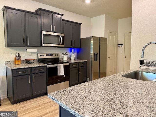 3836 Saddle Hill Way, Douglasville, GA 30135 - kitchen featuring appliances with stainless steel finishes, a sink, light wood-style flooring, light stone counters, and a textured wall