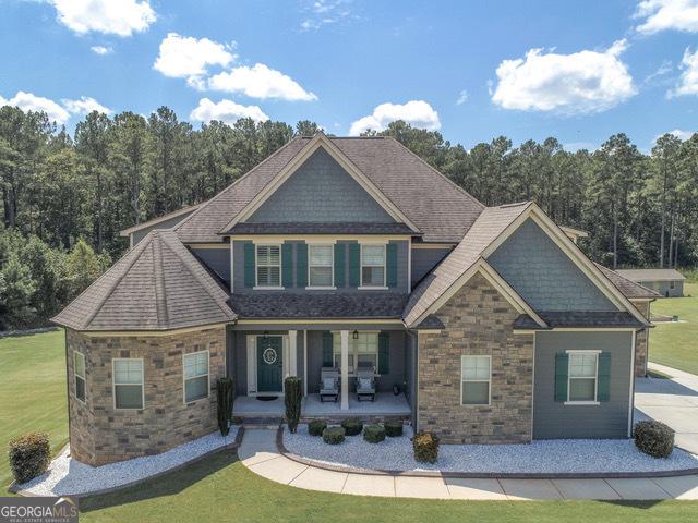 97 Senoya Ln, Senoia, GA 30276 - craftsman-style house with covered porch, stone siding, a front lawn, a view of trees, and roof with shingles