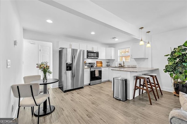 2912 Palm Dr, East Point, GA 30344 - kitchen with stainless steel appliances, a peninsula, white cabinets, light wood-style flooring, and a kitchen breakfast bar