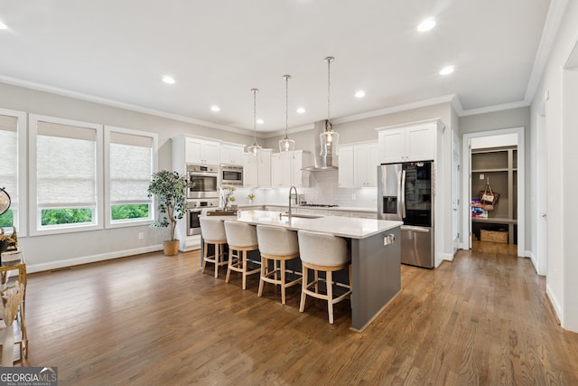 3998 Commodore Dr, Atlanta, GA 30341 - kitchen with appliances with stainless steel finishes, wall chimney exhaust hood, a kitchen island with sink, white cabinetry, and ornamental molding