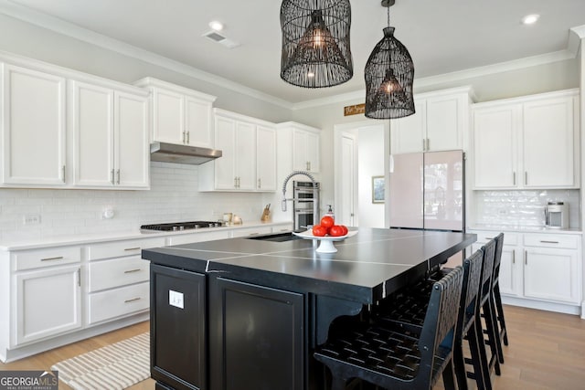 247 Widener Way, Peachtree City, GA 30269 - kitchen with freestanding refrigerator, white cabinets, a breakfast bar, under cabinet range hood, and an island with sink